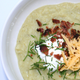 Bowl of thick potato leek soup with sour cream, bacon bits, and shredded cheese on top
